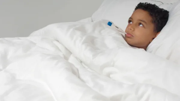 Child laying in bed with a thermometer in mouth