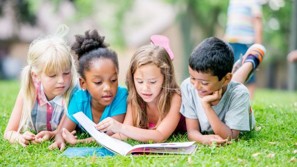 Four children laying on the grass and reading a book together