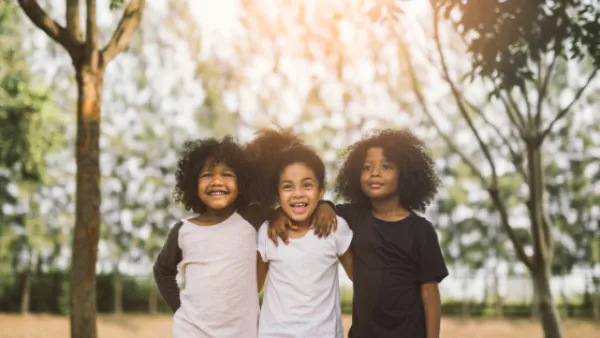 Three kids with their arms around each others shoulders smiling for picture